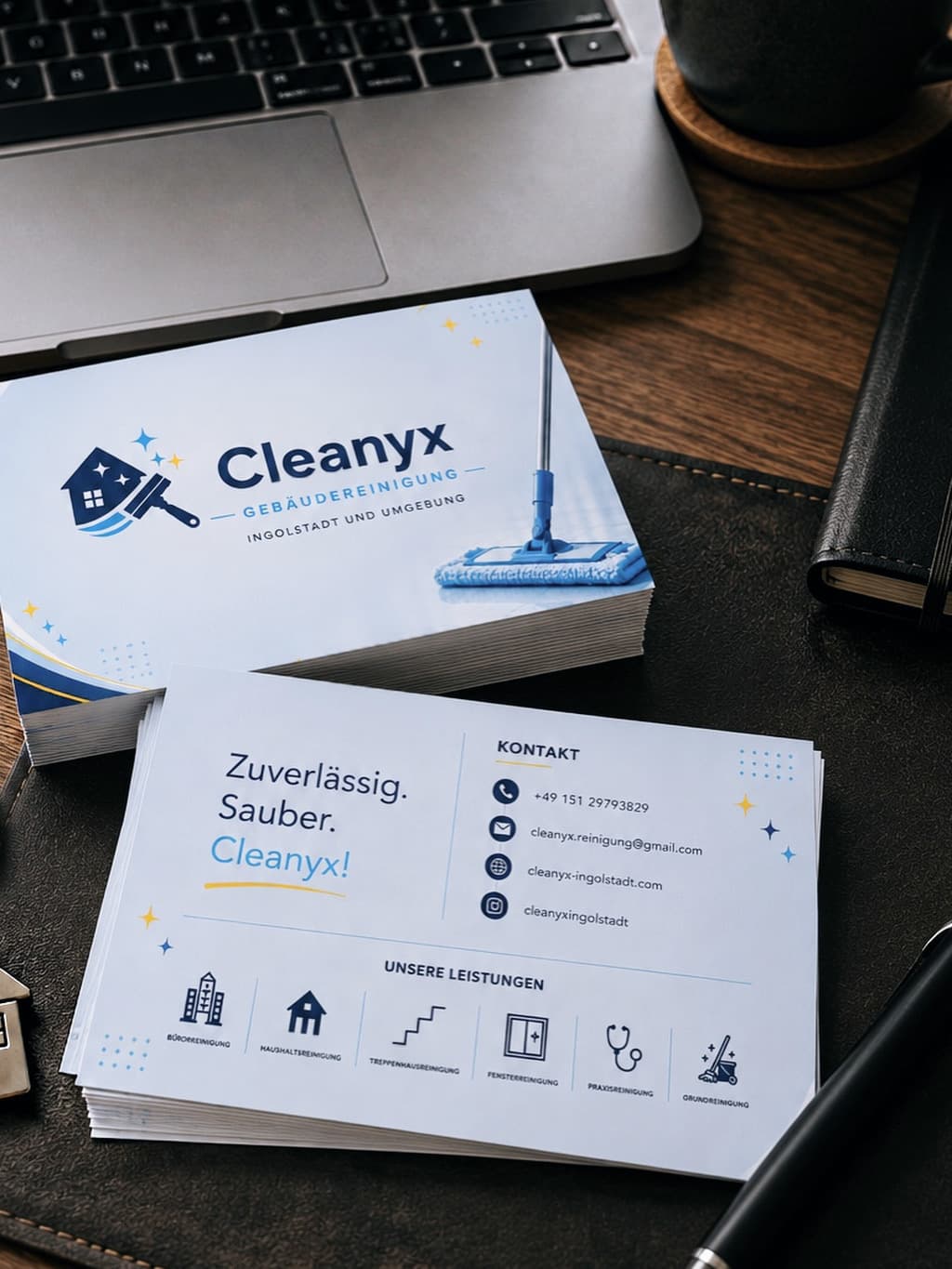 Visitenkarten von Cleanyx Gebäudereinigung mit Logo und Kontaktdaten auf einem Schreibtisch neben einem Laptop.