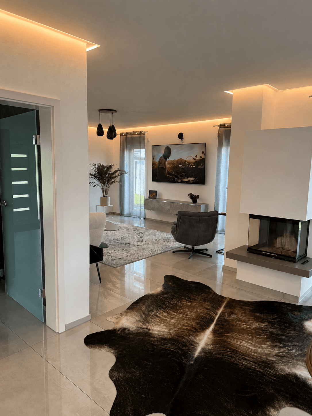Modernes Wohnzimmer mit Kuhfellteppich, Kamin, Fernseher und stilvoller indirekter Beleuchtung an der Decke.