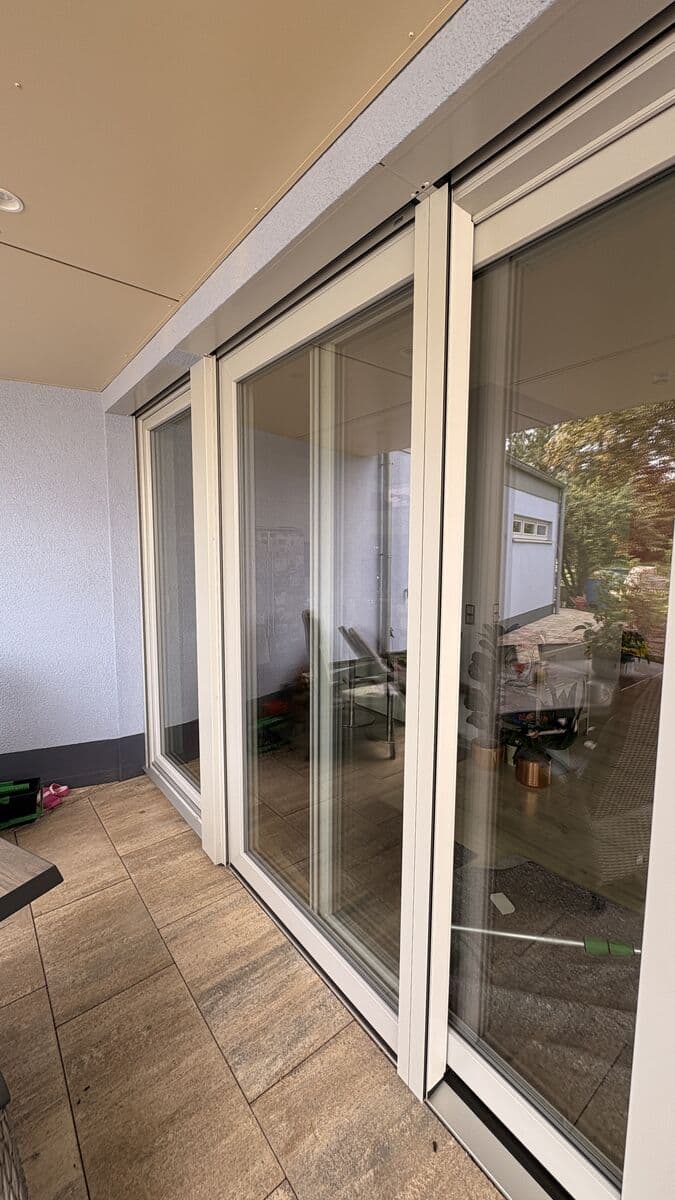 Große weiße Glasschiebetüren auf einer gefliesten Terrasse, die den Außenbereich und Bäume widerspiegeln.