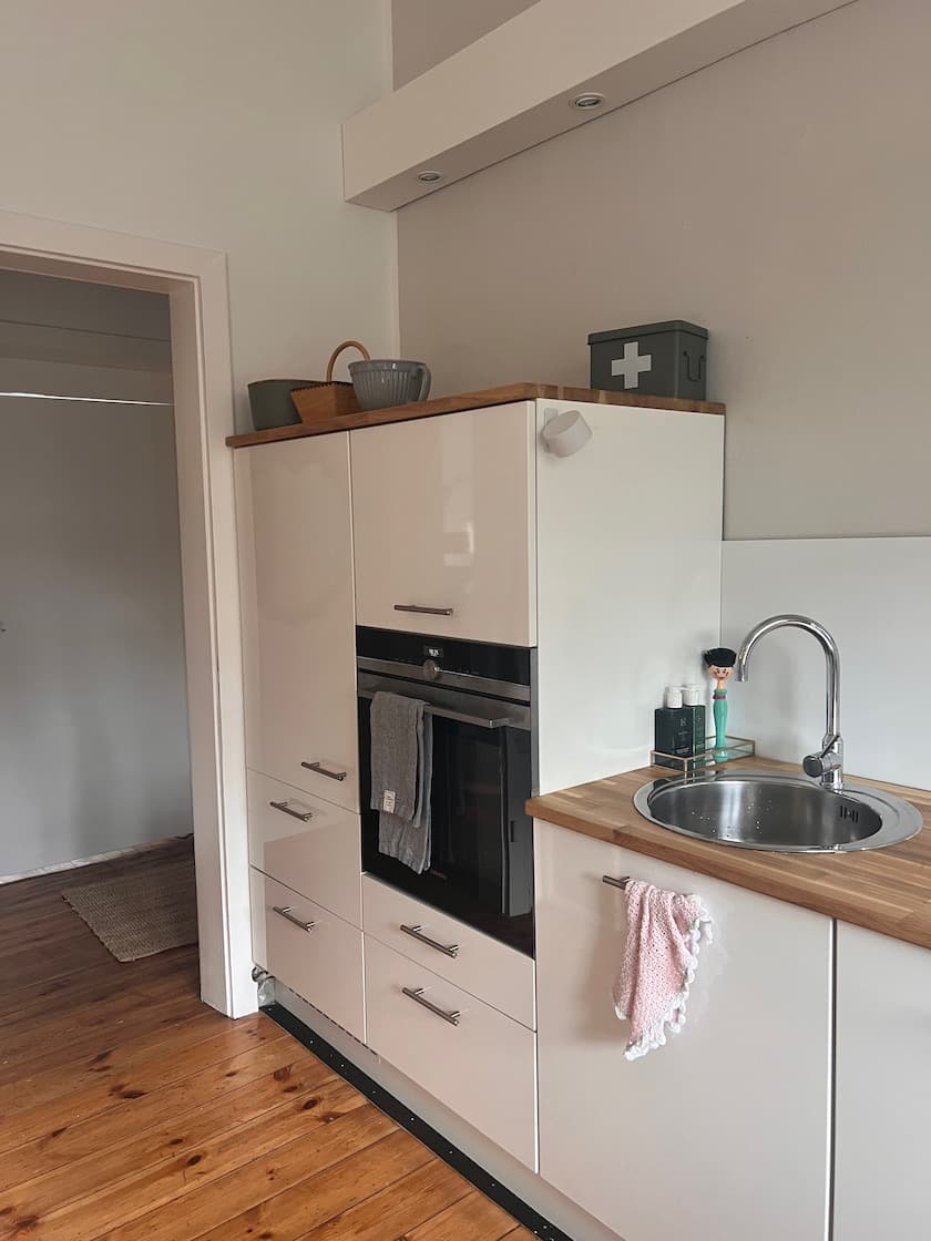 Moderne weiße Einbauküche mit Holz-Arbeitsplatte, Backofen und einem kleinen runden Edelstahl-Spülbecken.